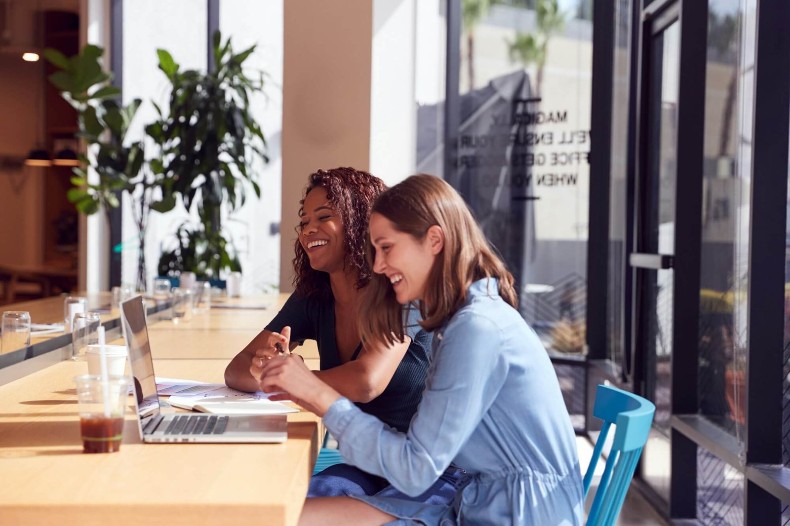 Two Businesswomen With Laptop At Desk By Window In Office Collaborating On Project Together