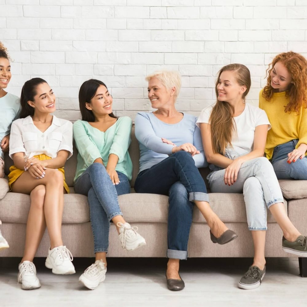 Multiethnic Women Looking At Each Other Sitting On Sofa Indoor